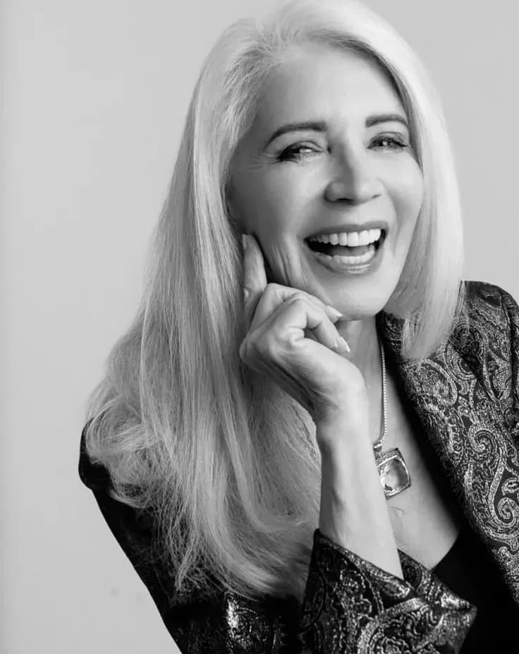 Ruth, founder of Go SILVR Goddess, laughing, her long silver hair loose over a paisley jacket